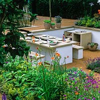 Sunken, outdoor dining area. Stone benches and table. Barbecue. Pots of herbs. Beds of daylily, alchemilla, lavender, agapanthus and herbs. Sunken.