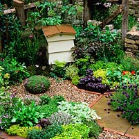 Beehive in herb garden surrounded by beds of lavender, mint, sorrel, pansy, angelica,  basil, thyme, fennel, chives, nasturtium, marjoram and parsley.