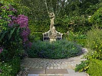 Marking the end of the long pergola, a circular stone courtyard, at its centre a bed of catmint and statue 'Sally'. On left, Eupatorium purpureum - hemp agrimony  with many butterflies.