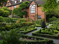 In a shady, sloping corner by the Arts and Crafts house, a recently established parterre of box and lonicera topiary and hedges, infilled with slate shards.
