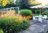 View of modern garden in late summer with miscanthus, persicaria, rudbeckias and table with parasol