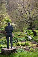 Statue of Dr. Jimmy Smart looking over valley bog garden and stream in Spring, Marwood Hill Gardens, Barnstaple, Devon, UK