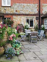 Secluded courtyard with table and chairs amidst pots of tree fern, hosta, Asiatic hybrid lilies, pelargonium and Fuchsia 'Mrs. W Rundle', standard F. 'Celia Smedley'.