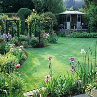 Raised summerhouse and herbaceous perennials with American iris. Large pergola fills left corner.