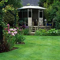 Raised summerhouse with planting of hosta, alchemilla, iris, rodgersia, American irises and Rosa Alchymist.
