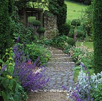 Old wooden gate at end of nepeta-lined path edged in box and holly topiary, Italian cypress, foxglove, eremurus, phlomis, peony, stachys and corydalis. Path laid from white stones dug out from garden, interspersed with old reclaiimed setts.