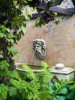 In a shady garden corner, horse trough wall fountain with Nepture's head from Triton stone
