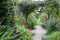 View into Sundial Garden framed by clematis covered pergola, heleniums, monardas, agapanthus and salvias, with asters full of buds beyond. Wollerton Old Hall, nr Market Drayton, Shropshire, UK