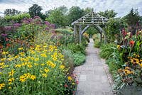 Path through the Lanhydrock Garden, otherwise known as the hot garden, passes below a wooden pergola surrounded by Ligularia dentata 'Desdemona', stripey cannas, rudbeckias, eupatorium and heleniums. Wollerton Old Hall, nr Market Drayton, Shropshire, UK