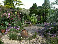 A circular themed gravel garden and patio with cottage garden style borders. Planting includes Pimpinella major Rosea, Rosa Mundi, Geranium nimbus and Dianthus, with Armeria Joystick in the centre of the gravel bed. 