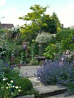 A small circular patio in the middle of a gravel garden. Privacy is created by the surrounding planting which includes Rosa Mundi, Nepeta Six Hills Giant, Geranium Nimbus, Buxus sempervirens and Stipa gigantea.