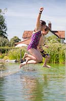 Boy and girl jumping into a natural swimming pond.