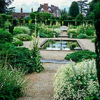 Formal pond in the White Garden with verbascum, Tanacetum niveum, hebe, hydrangea, hosta, rose and bamboo. Behind, Elizabethan manor house.
