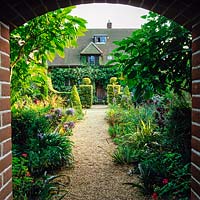 Walled Entrance to 1913 Arts and Crafts house, seen through brick arch past agapanthus and box topiary hedges.