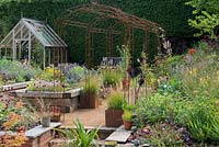 Rusty iron pergola divides garden of raised beds and border of late summer flowering perennials.