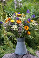 Galvanised jug filled with arrangement of herbal plants - feverfew, marigold, clary sage, oregano, mint, rosemary, lavender.