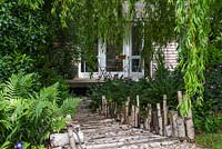 Walkway crafted from lengths of birch by Claire Knights, sculptor. Beneath willow, shady bed of hardy geranium, tiarella and fern. 