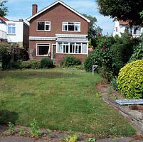 Before shot of rear of 1960s riverside home wedged between its neighbours. Dull red brick, ill proportioned windows and low-pitched gable need updating.