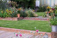 A brick step ascends from deck to lawn. Beyond, steps beside a raised bed of Echium plantagineum, catmint, coneflower, annual poppies, nasturtium, lavender, Stipa tenuissima and oriental lilies.