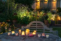 A table with candles and a backlit border illuminate a garden at night.