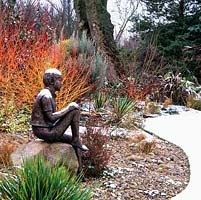 Boy statue on snowy rock, behind, red Salix var. vitellina Britzensis.