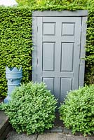False grey door -  trompe l'oeil illusion set into the yew hedge, framed by grey painted flower pots and loosely clipped box. Tony Ridler's garden, Swansea, Wales, UK