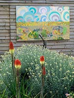 A picture, created by Liz Shackleton, hangs in the garden behind a bed of Kniphofia 'Atlanta' and Helichrysum Italicum