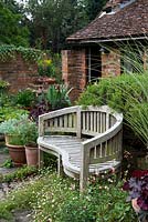 A wooden bench surrounded with Erigeron karvinskianus and Salvia 'Hot Lips'.