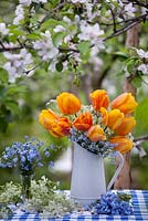 Floral arrangement with tulips, cow parsley and forget-me-nots on the table under a flowering apple tree.