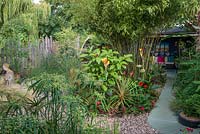 A small town garden with tropical foliage plants including bamboo with path leading to a secluded seating area.