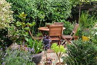A wooden table and chairs on a secluded patio surrounded with containers planted with Magnolia, Agapanthus, Aeonium and Lavandula