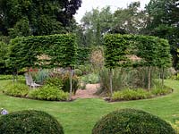 A round gravel garden cut out of a sunny lawn, encircled by a pleached hornbeam hedge. Summer.