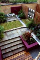 Modern city garden with a water spout into a stainless steel rill, surrounded by paving, patio, grass and stone steps. Designed by Paul Dracott.