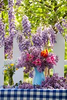 Outdoor spring display. Flowering Wisteria. Jug of tulips and syringa. Forget me nots and buttercups in a vase.