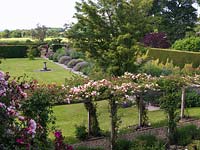 View from upstairs of pergola bearing climbing roses American Pillar and pink Albertine herbaceous border backed by leylandii hedge and unspoilt countryside beyond.