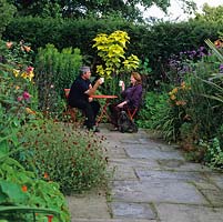 Chris and Sheila Bissell take a break in the hot garden with Digby, a Cairn terrier. Beds: Verbena bonariensis, nasturtium, Lilium African Queen, canna, daylily, catalpa.