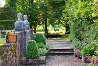 Brick path and steps alongside retaining wall with pair of Greek sphinx stone statues, clipped box and yew topiary