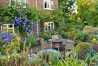 Planting includes: bed by house - Lonicera 'Baggesen's Gold', Clematis 'Perle d'Azur', Venosa Violacea, Geraniums 'Rozanne' and 'Ann Folkard'. In raised bed: Buxus, Santolina chamaecyparissus, Sedum 'Matrona', Eryngium 'Big Blue', Panicum 'Rotstrahlbusch', Ophiopogon plansicapus 'Nigrescens', Oenothera missouriensis, Morinia longifolia'
