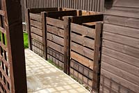 Three bay wooden compost bins located behind a timber trellis 