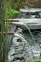 The Great Chelsea Garden Challange Garden. Water feature with slate walls, paving, channel and pipe fountains.  RHS Chelsea Flower Show, 2015
