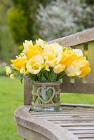 Floral display of Tulipa 'Sunny Boy', Tulipa 'Creme Lizard', Tulipa 'Golden Apeldoorn' and Cheiranthus cheiri 'Ivory White' in glass vase