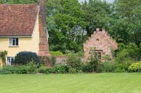Old Suffolk house with large brick chimney, Ceanothus and newly built brick house with a crow stepped gable. Heveningham, June