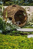 Living Landscapes 'City Twitchers' - view across pond and circular paved areas towards spherical willow bird hide and nesting box with mixed white planting - RHS Hampton Court Flower Show 2015