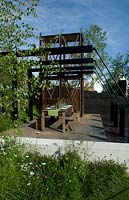 Table set in garden constructed from remains of industrial landscape of an old coal mine complete with winding shaft and heavy steel girders. Hadlow College Green Seam garden. Encroachment of wild planting and birch tree. 