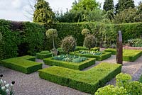 Box Parterre with central beds planted with Elaeagnus x ebbingei lollipops above 'Ivory Giant' wallflowers, santolina and Tulipa 'Spring Green' and 'Queen of the Night'. In pots, lollipop variegated holly. Sculpture by Matt Stein.