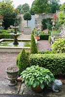 Formal courtyard garden behind Georgian terraced house with central water feature, box edged beds infilled with Japanese anemones, echinops and roses, box cones, stone urns, a standard bay and containers planted with succulents and hostas.