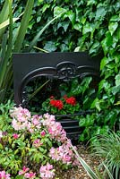 Tucked away by ivy covered fence, the cottage's original fire surround, flaming geraniums in its grate. Surrounded in phormium and pink azalea.