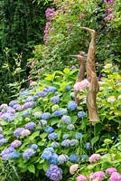 Three long shaped ceramic birds next to Rosa 'Veilchenblau' and Hydrangea macrophylla 'Endless Summer'