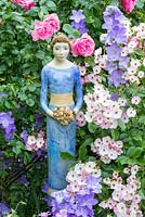 Blue ceramic lady holding a flower bouquet next to Rosa 'Ballerina', 'Leonardo da Vinci', Buxus and Campanula persicifolia var. sessiliflora