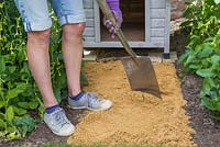 Filling the excavated channel with sharp sand, as a base to ensure the stone path remains sturdy and in position